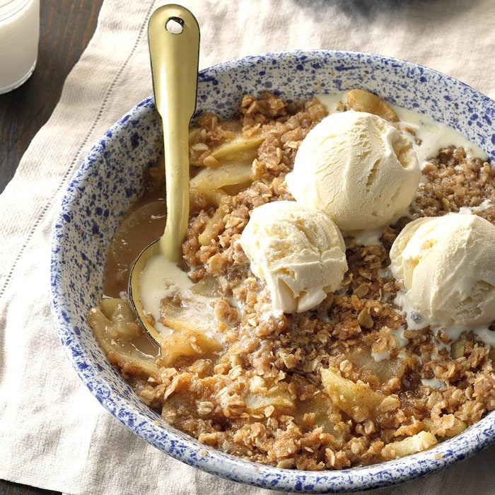 An apple crisp in a bowl with vanilla ice cream on top with a spoon.