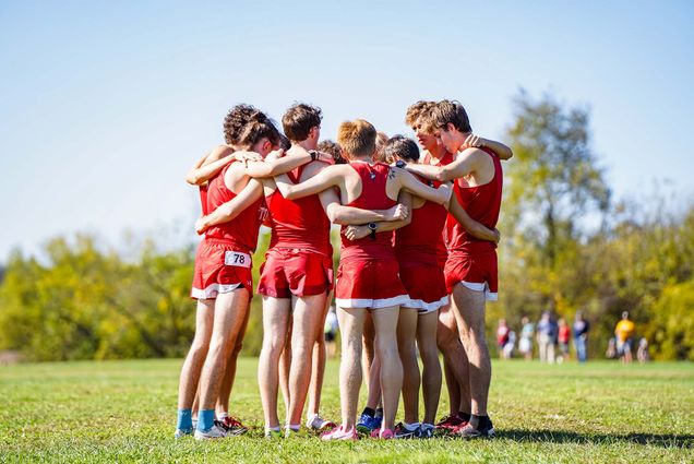 Photo: A group of men's cross country runner in red uniforms huddle at a recent meet
