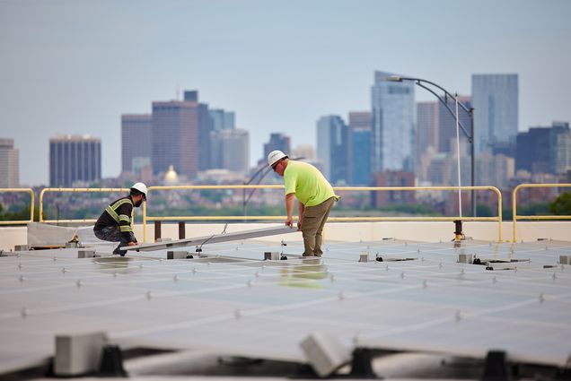 Photo: Workers install solar panels on the top of a large BU Building in Boston, MA