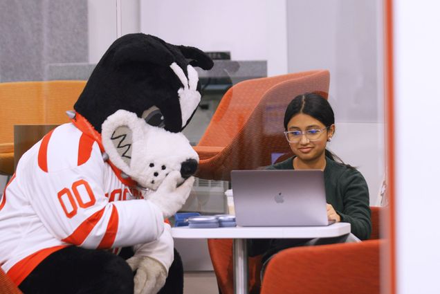 Photo: Boston University's mascot Rhett, a Boston terrier, and a female student sitting next to one another at a table and looking at a laptop