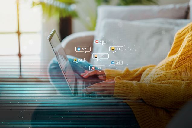 Photo: A person on their couch browsing social media on their laptop. Icons are coming out of hte computer showing likes and engagement with posts. There is a glitch overlay on the image