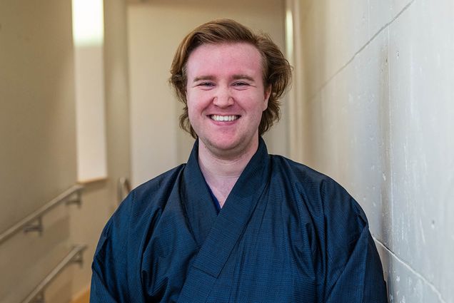 Photo: CFA senior Chris Ellars, a young white man wearing a traditional navy kimono, smiles for a photo.