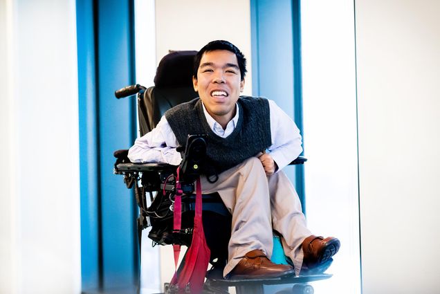 Photo: PhD student Justin Moy smiles for a portrait photo in a vest and white button up