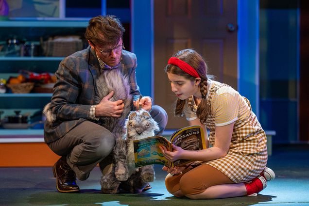 Photo: A man on the left controlling a squirrel puppet as a young girl on the right shows it an open magazine