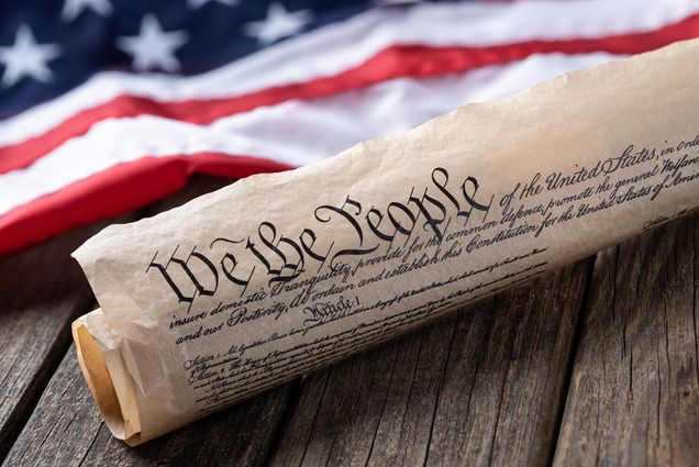 Photo: United States constitution with American flag in background on rustic wooden table