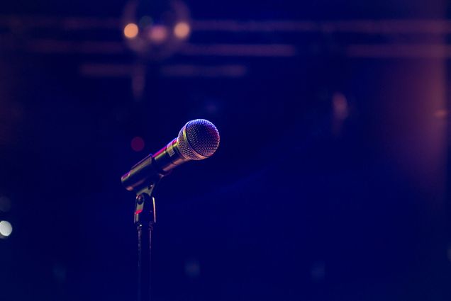 Photo: A stock image of a mic on stage with blue, purple lighting.