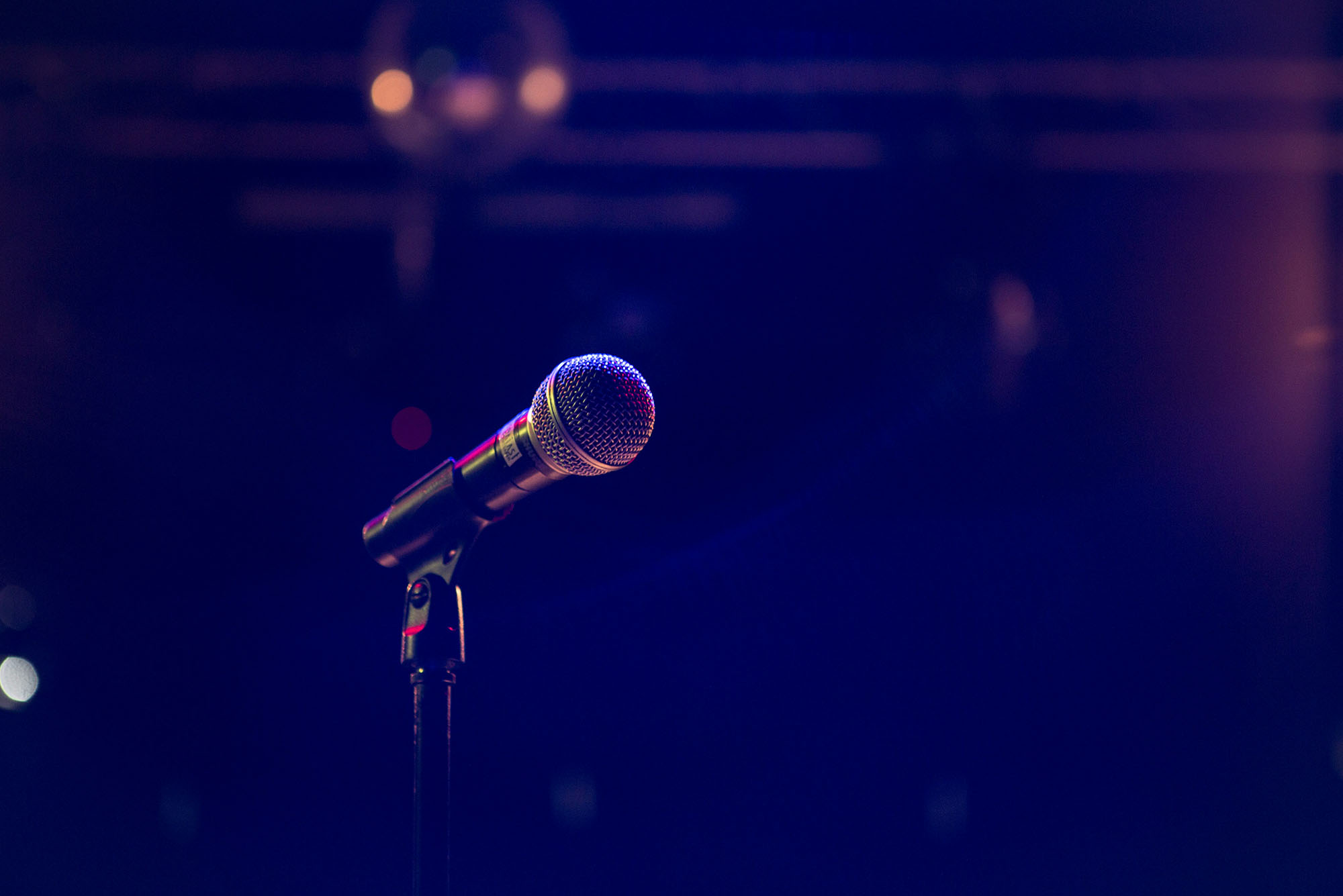 Photo: A stock image of a mic on stage with blue, purple lighting.