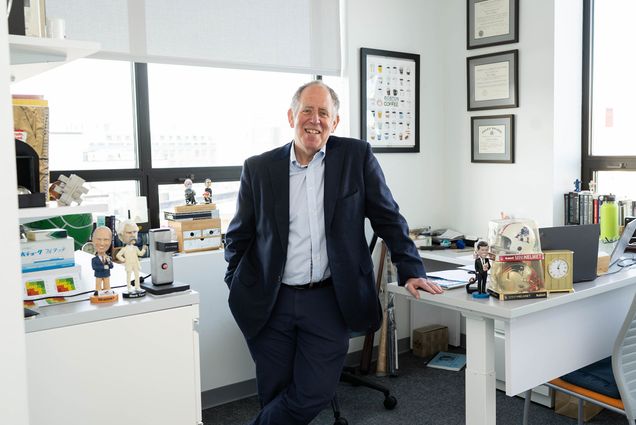Photo: A white man with a smile wearing a suit stands in front of an office full of fun trinkets
