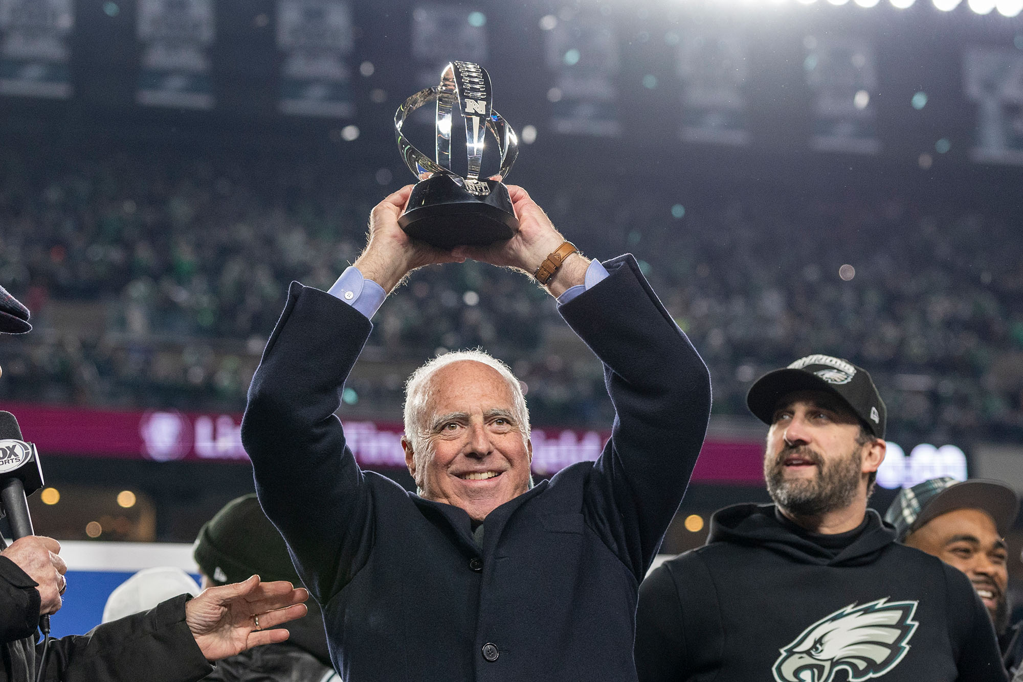 Philadelphia Eagles owner Jeffrey Lurie hoists the George Halas Trophy after the NFC Championship NFL football game against the Washington Commanders, Sunday, Jan. 26, 2025, in Philadelphia. The Eagles defeated the Commanders 55-23. Photo by Lauren Bacho via AP