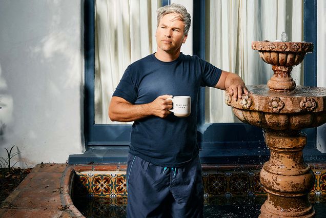Photo: A man with gray hair wearing a blue tshirt, holding a coffee mug, and standing inside a fountain