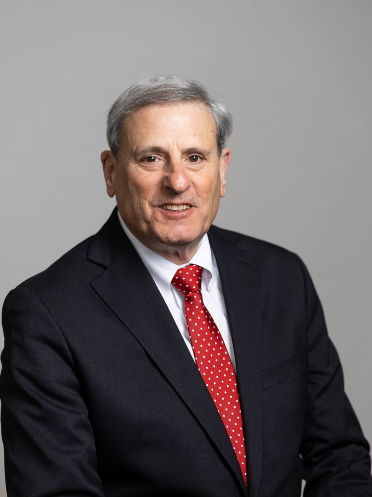 Photo: A man smiling for a portrait while wearing a dark suit and vibrant red tie