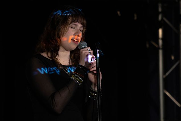 Photo: A young woman with piercings sings at an open mic while the lyrics are projected over her face.