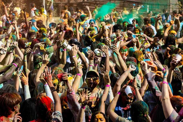 Photo: A crowd of people with many colors surrounding them at a Holi celebration