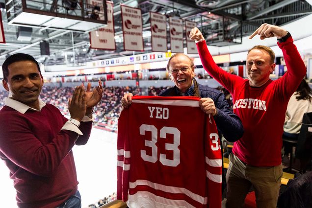 Photo: A 91-year-old man holding up a BU Hockey jersey with his name on it as two men next to him celebrate