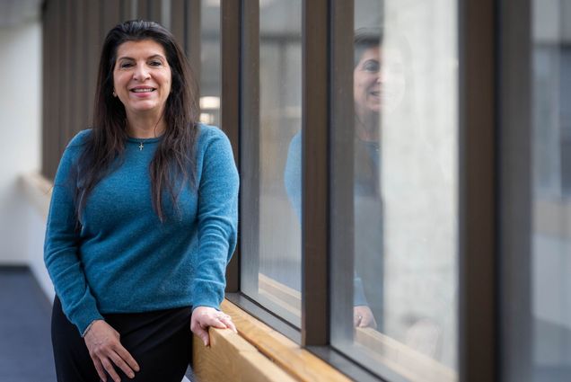 Photo: A woman with long dark hair in a blue shirt poses for a headshot portrait in a well light room