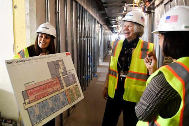 Photo: Three women in hi-vis vests and wearig construction hats review a large floorplan on a construction site