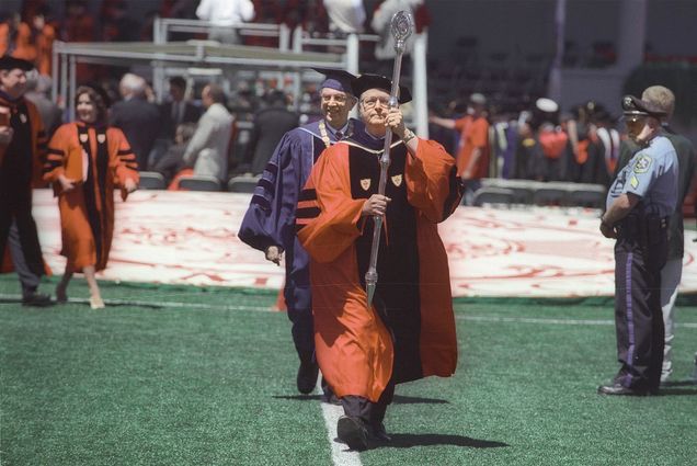 Photo: An older gentleman in graduate regalia marches with Mace at Boston University's Commencement ceremony.