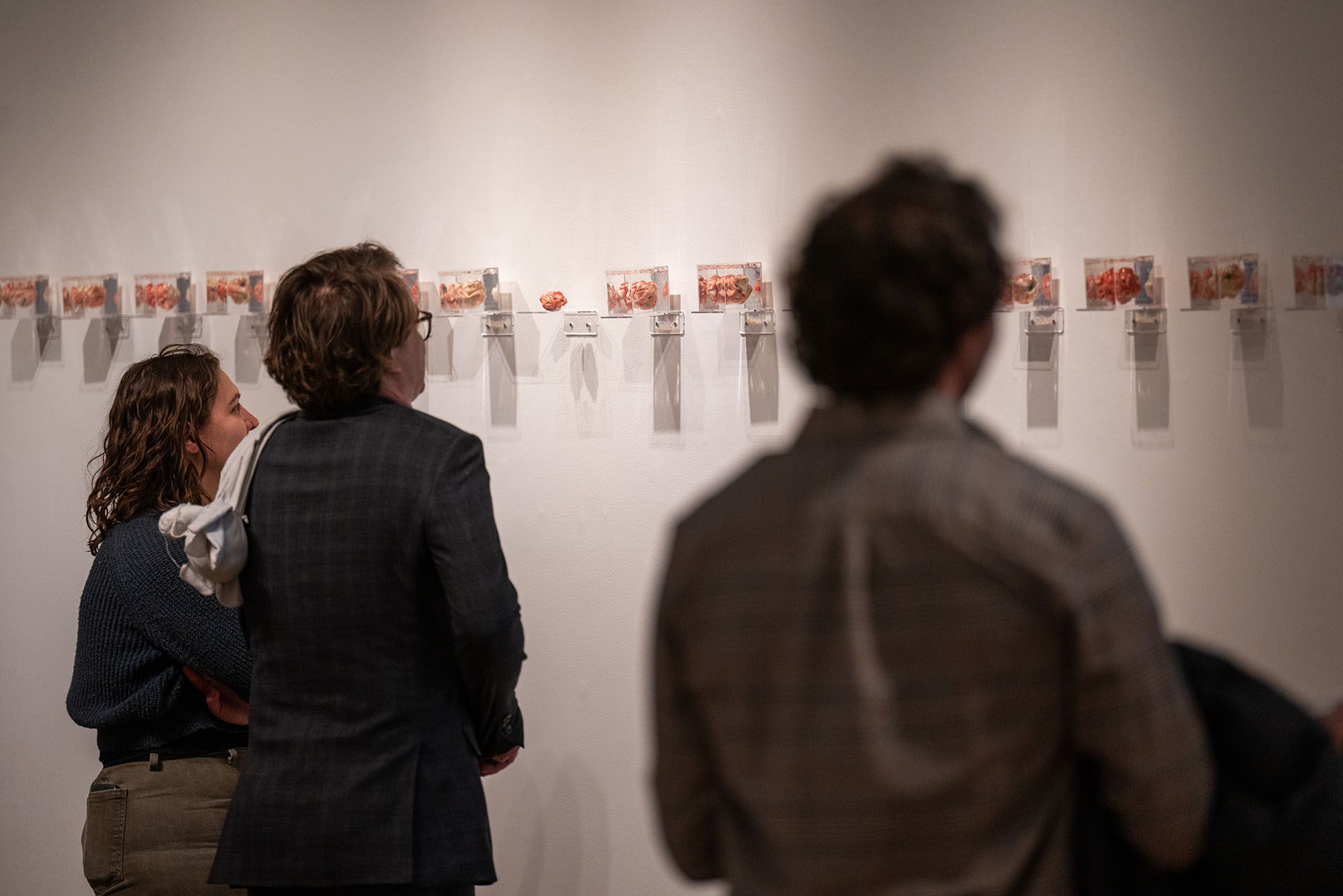 PHoto: Small cermamic figures mounted in a line on a wall at a Sculpture thesis exhibit