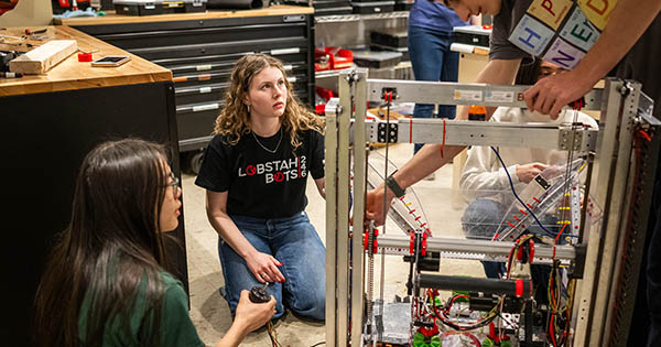 Photo: A young woman helps high school kids with their robotic project.