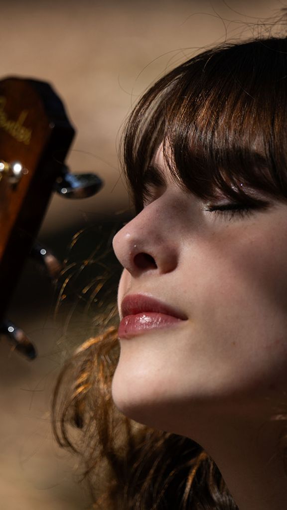 Photo: A girl holding a guitar outside with her eyes shut as the sun casts shadows on her face