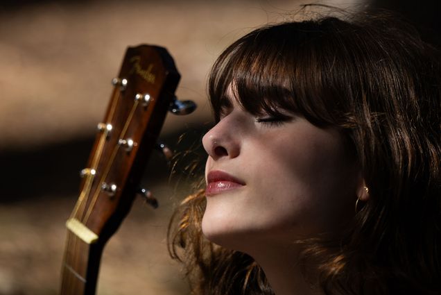 Photo: A girl holding a guitar outside with her eyes shut as the sun casts shadows on her face
