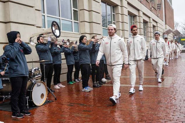 Photo: Group of BU hockey players in all white track gear walking on the sidewalk.