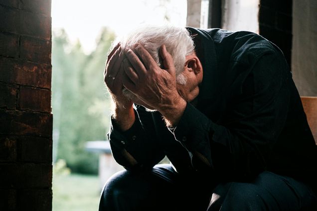 Photo: An older man with white hair and his head in his hands