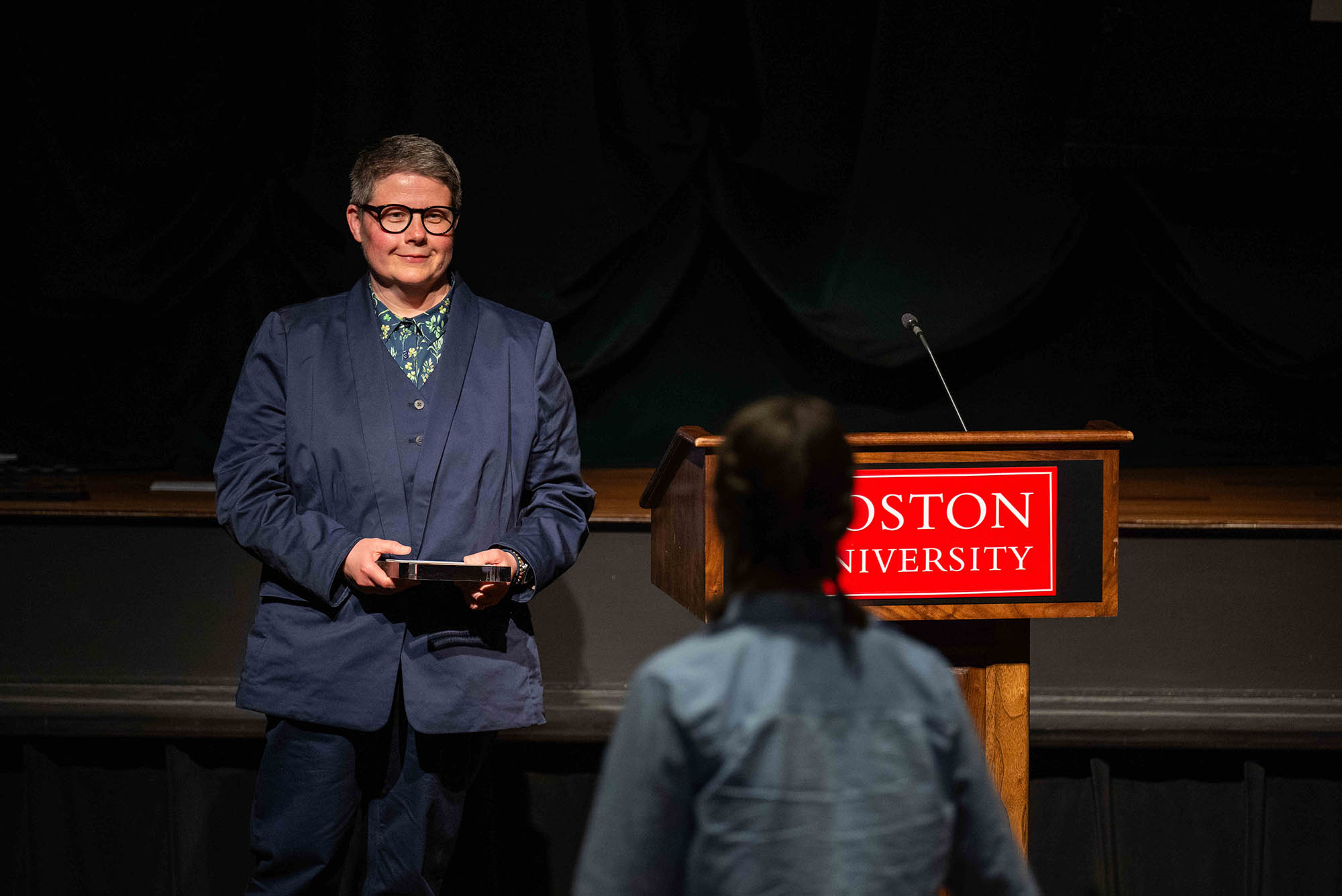 Photo: An older woman wearing a suit talking at a podium.