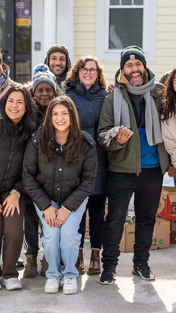 Photo: A group of people smiling and posing while wearing winter jackets outside of a building