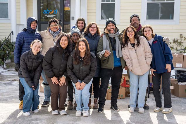 Photo: A group of people smiling and posing while wearing winter jackets outside of a building