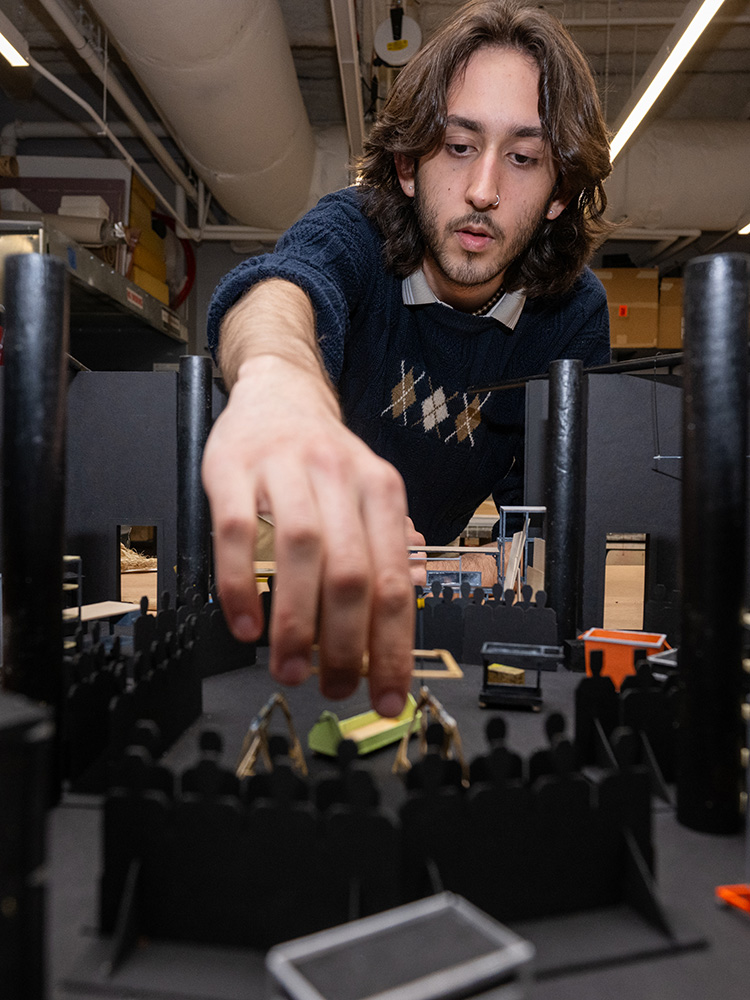 Photo: A man with long dark hair puts together a model set for a play at Boston University