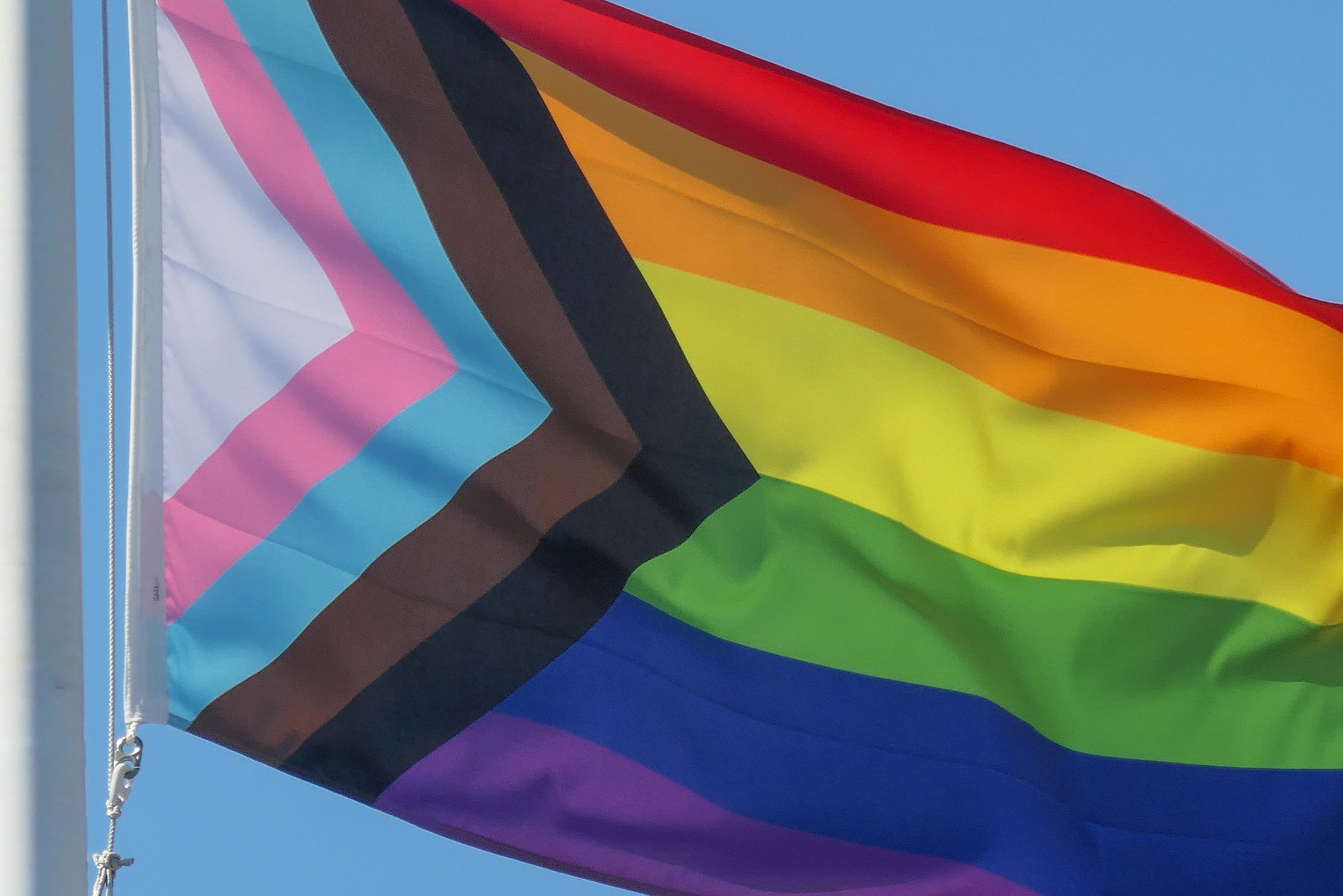 Photo: A picture of a pride flag being raised in front of a blue sky