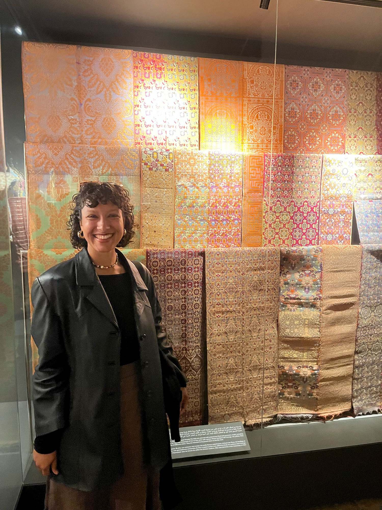 Photo: A girl in a leather jacket smiling in front of textiles