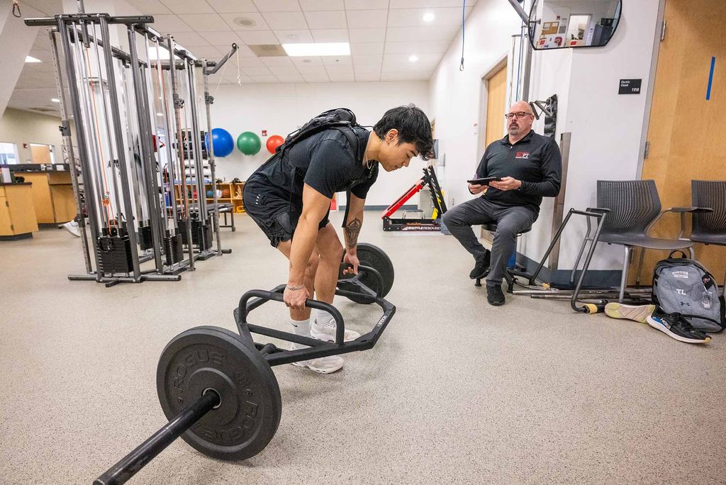 Photo: A young man with a mechanical contraption on his back to assist with his deadlifts.