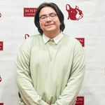 Photo: A young man with chin length black hair poses for a photo in a green sweater.