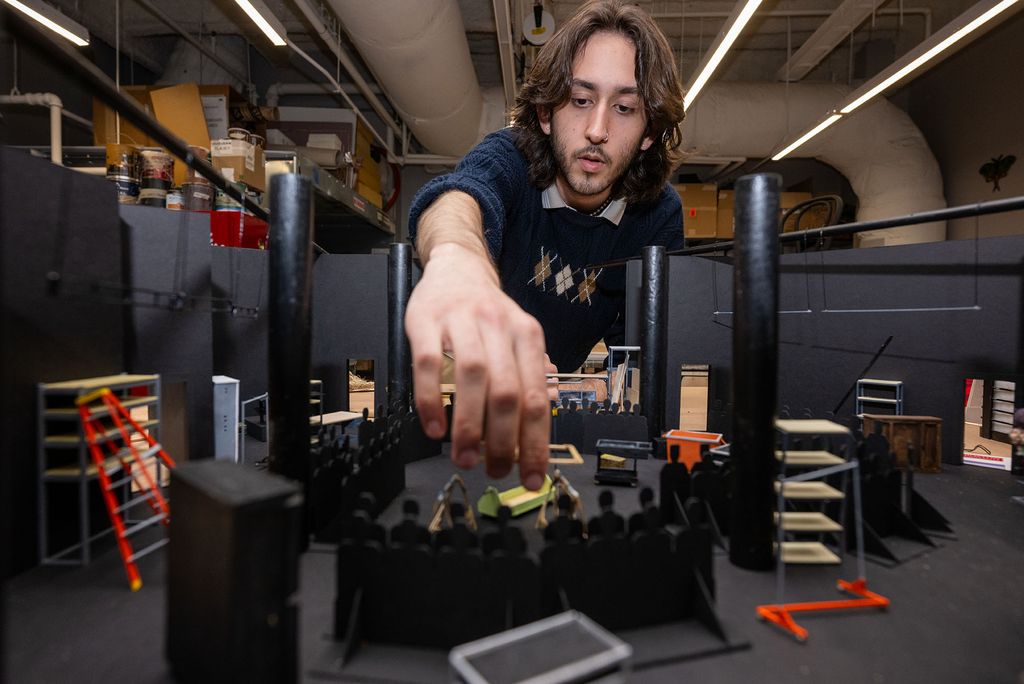 Photo: A man with long dark hair puts together a model set for a play at Boston University