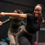 Photo: A woman in the foreground dancing with a few other people in the background. Her arm is extended and she is smiling