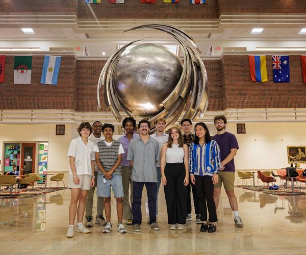 Cohort of students posed in front of a large metal statue in a building atrium