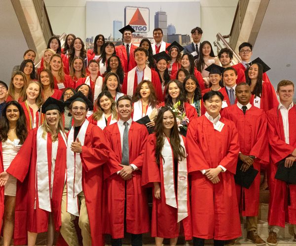 Large cohort of students in graduation gowns standing together in a stairwell