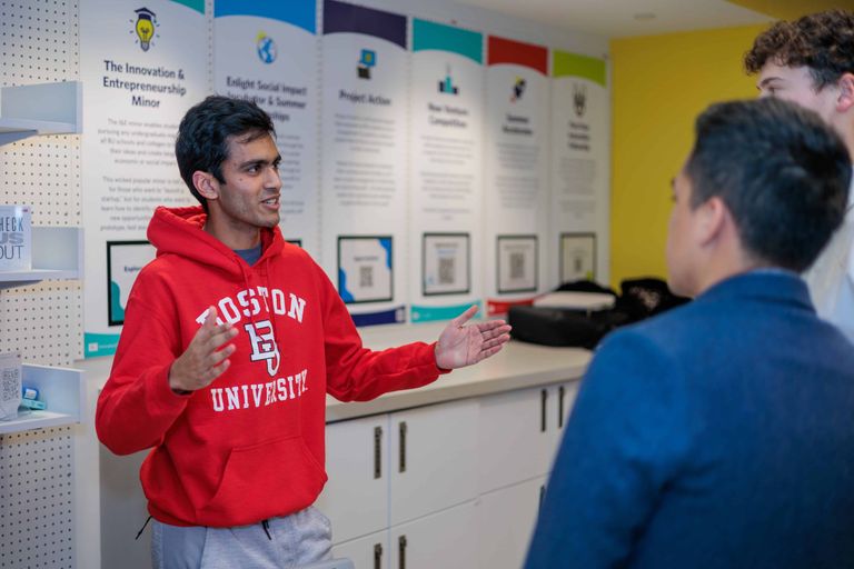 Man gestures with his arms while speaking to two other students