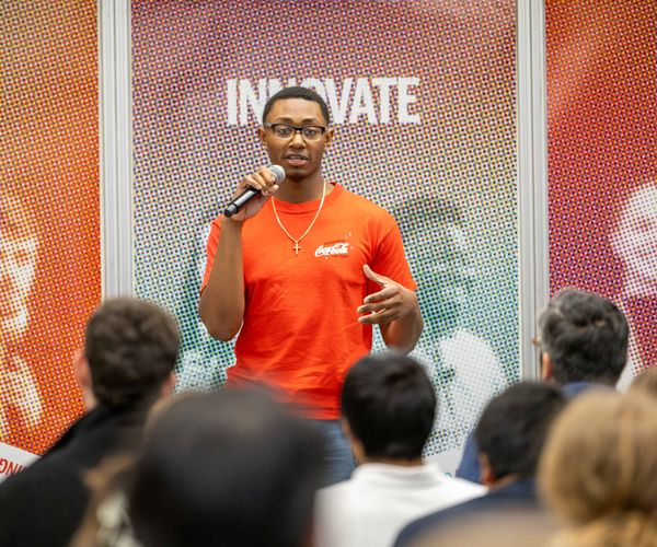 Student presenting in front of a colorful backdrop and holding a microphone