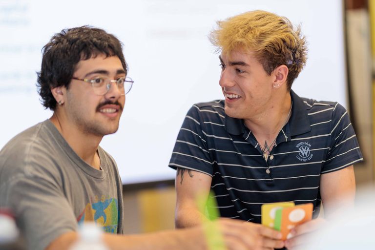 Two students smiling and laughing seated at a table