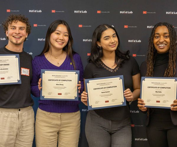 Group of four students smiling holding certificates in front of a backdrop