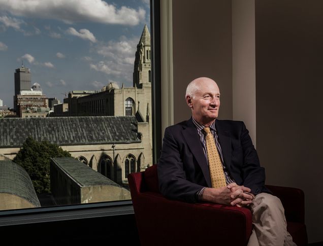 Professor Robert Volk sits in a red chair with the BU School of Theology in the background