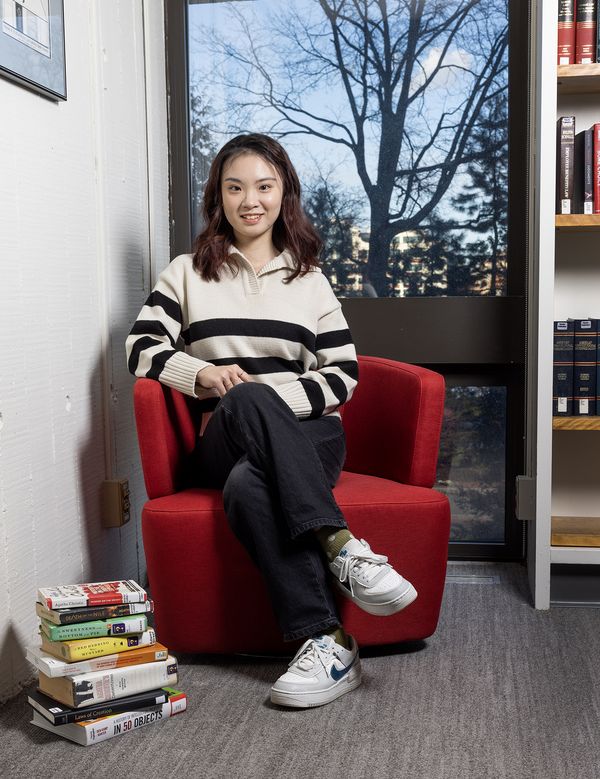 Zhuoming Yuan, LLM Class of 2023, sits in a red chair with books stacked next to her