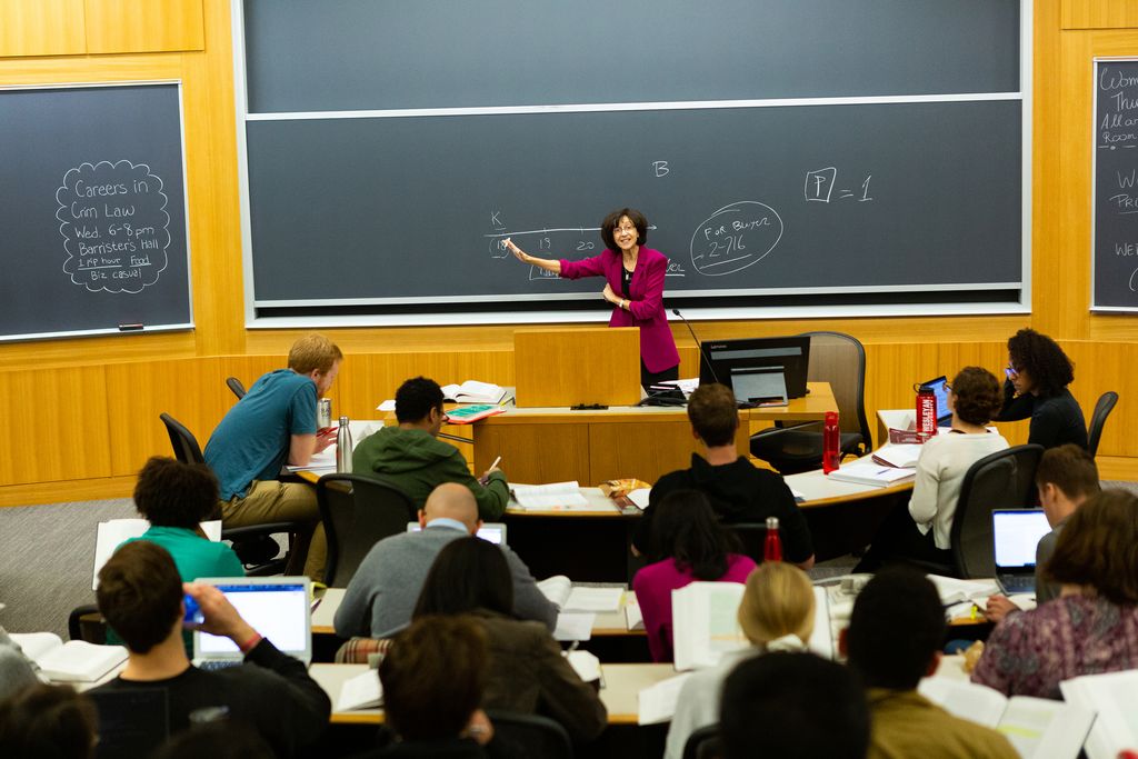 Professor Daniela Caruso gestures to the blackboard at the front of a classroom in the Redstone building