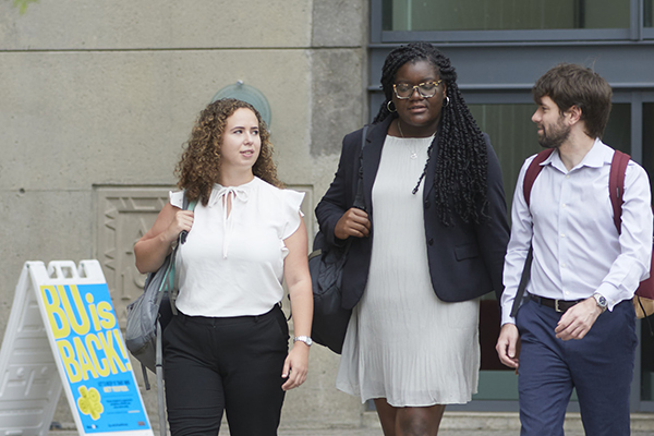Three students carry backpacks and walk together outside the law complex.