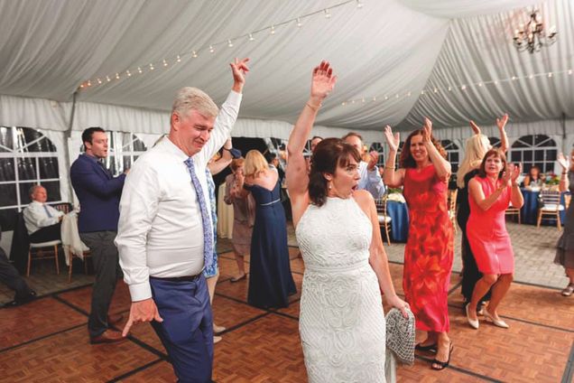 Boston University School of Law alumni, Christine Desmarais Bergstrom, dances with Jack Bergstrom at their wedding as guests dance and clap in the background.