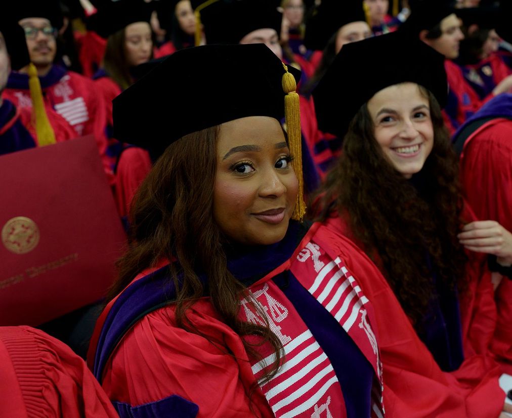 A student with long hair wears red regalia at Commencement.