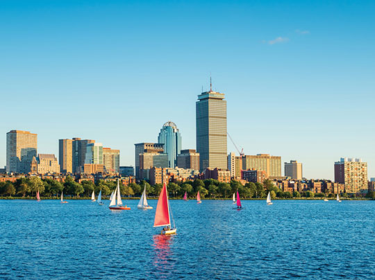 A sailboat on a sunny day crossing the Charle's River with the city of Boston in the background.
